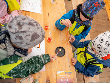 Kinder führen mit Pipetten und farbigen Flüssigkeiten Experimente zu Formen und chemischen Reaktionen durch.